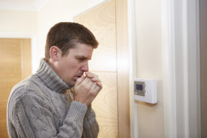 Man is cold because furnace is blowing cold air and he is checking the thermostat