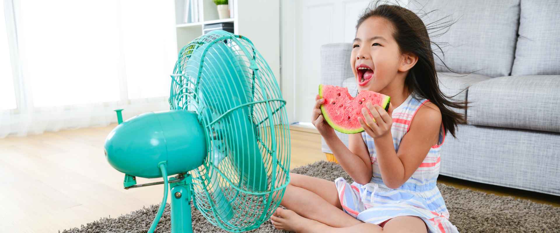 girl sitting by fan eating watermelon to stay cool